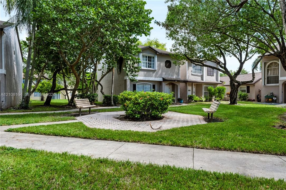 Exterior grounds featuring paved walkways, a central stone-paver hardscape, mature landscaping, and outdoor seating