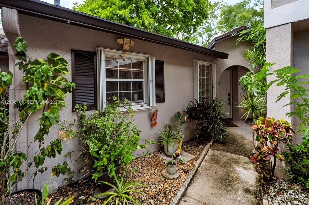 Stucco exterior featuring dark-toned window shutters, an arched entryway, and a concrete pathway