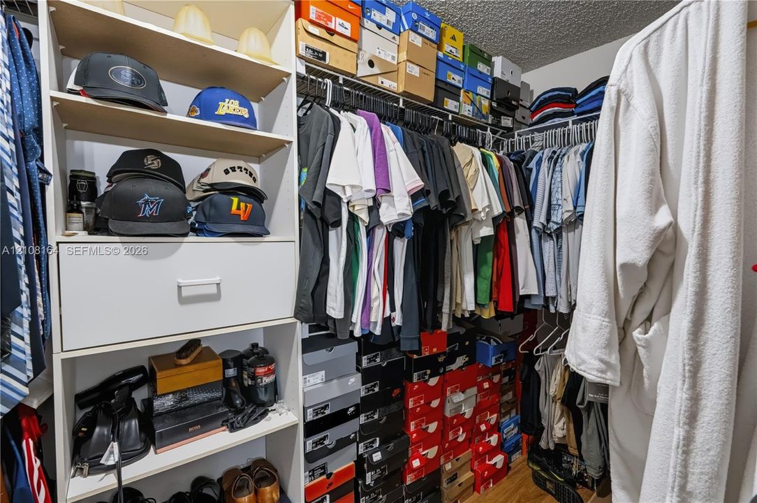 Walk-in closet featuring white laminate built-in cabinetry, an integrated pull-out drawer, adjustable open shelving, and multi-level metal hanging rods