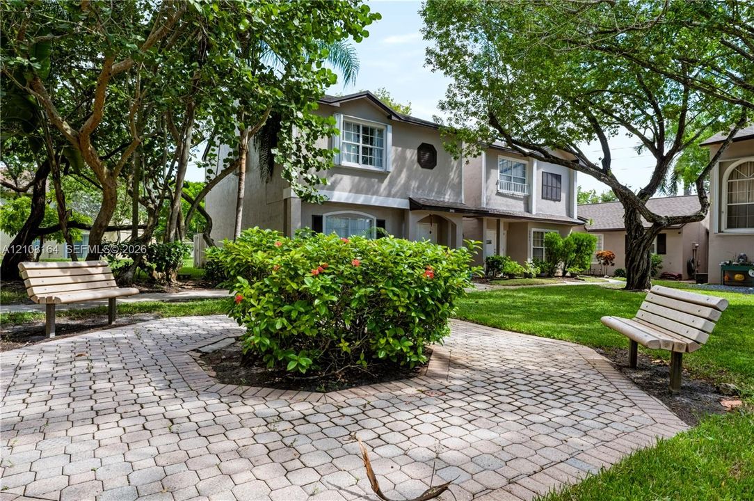 Paver-stone walkway featuring established landscaping, mature shade trees, and a manicured lawn