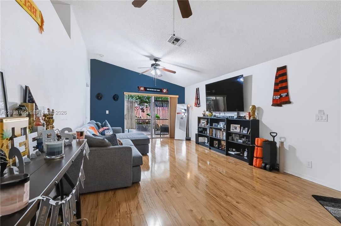 Living room featuring vaulted ceilings, wood-finish flooring, two ceiling fans, and a sliding glass door