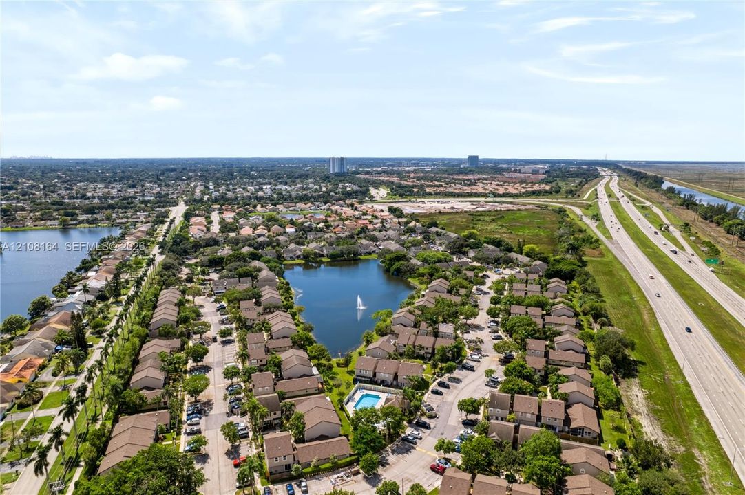 Aerial perspective of a residential community featuring a central lake, a swimming pool, and extensive mature landscaping
