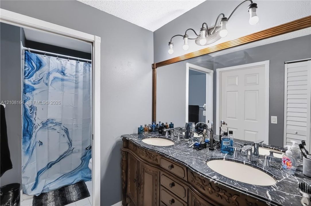 Custom wood cabinetry with ornate detailing, dual under-mount sinks, stone-finish countertops, full-width wall mirror with wood trim, and multi-light vanity fixture