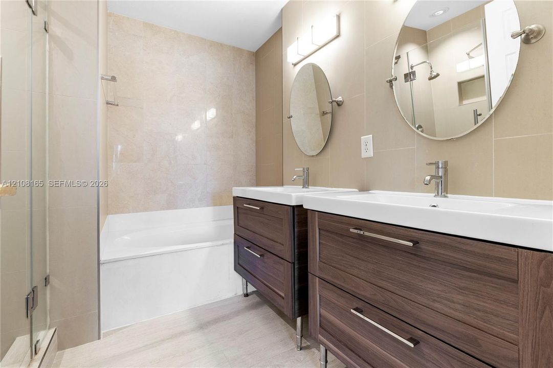 Dual-sink floating vanity with wood-finish cabinetry, rectangular porcelain basins, and polished metal fixtures paired with a porcelain tile shower surround and tub enclosure