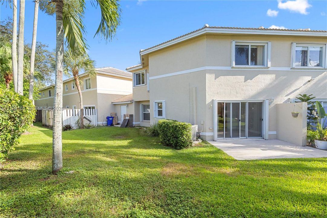 Stucco exterior featuring a concrete rear patio, sliding glass doors, horizontal windows, and a landscaped lawn with palm trees