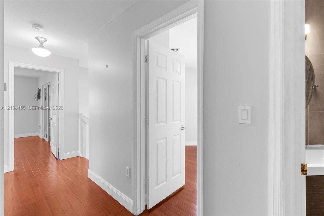 Hallway featuring wood-finish flooring, six-panel interior doors, and a semi-flush mount light fixture
