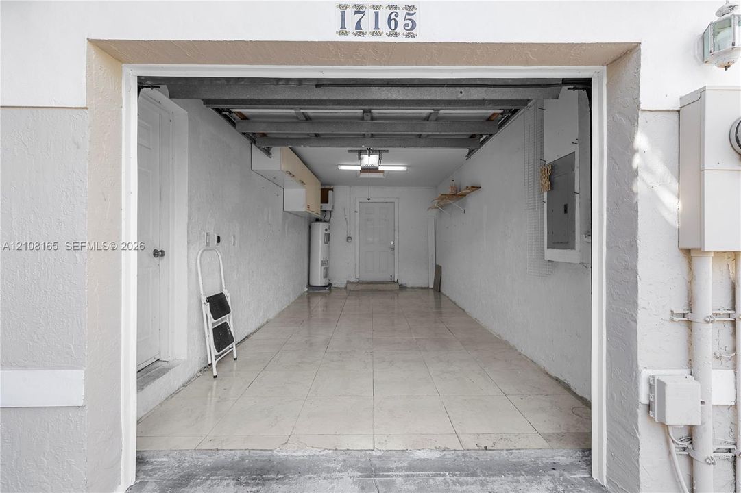 Single-car garage featuring tiled flooring, built-in shelving, a water heater, and interior access door