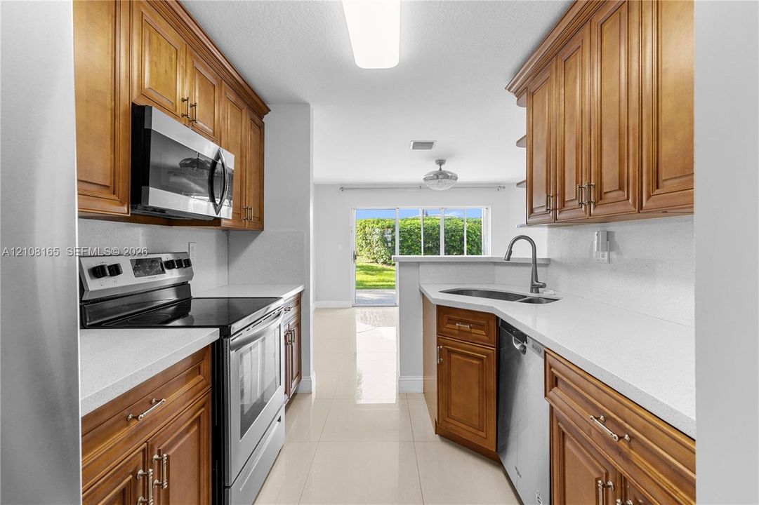 Kitchen featuring solid wood cabinetry, stainless steel appliances, solid surface countertops, an undermount sink with a gooseneck faucet, and tile flooring