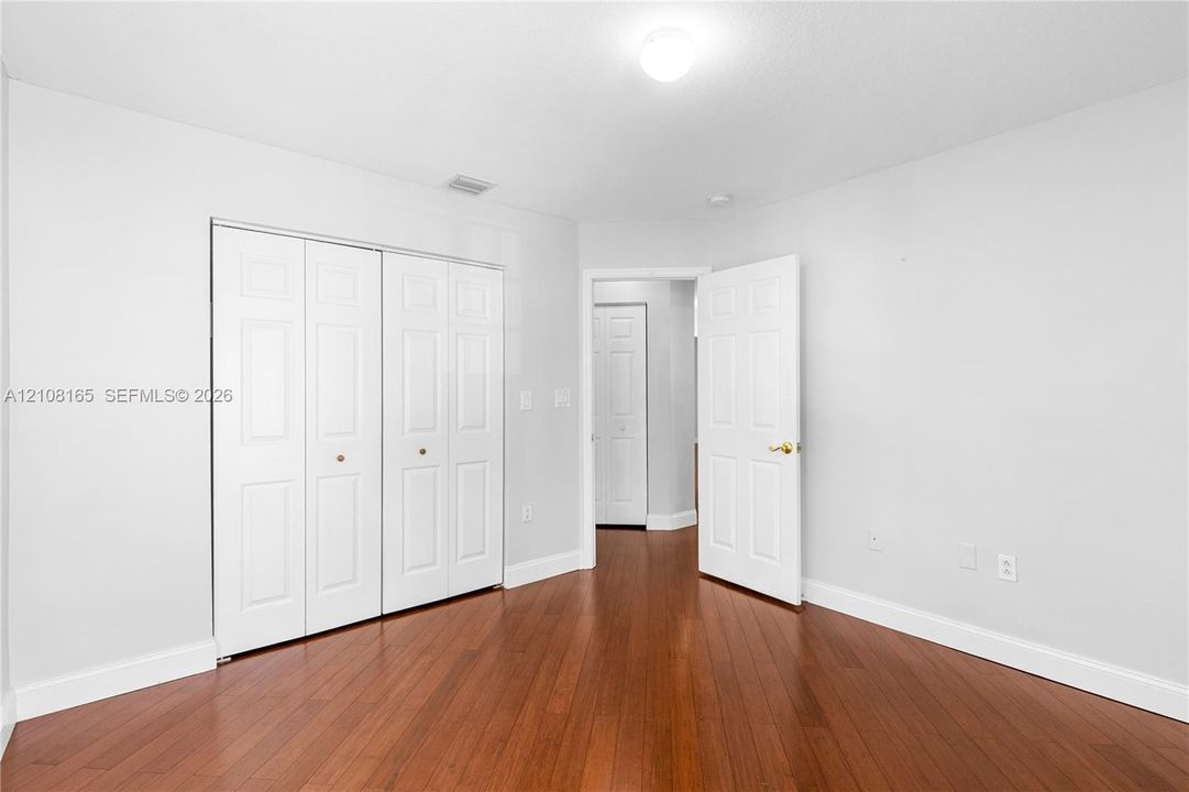 Room featuring wood-finish flooring, white walls, two sets of bifold closet doors, and a six-panel interior door