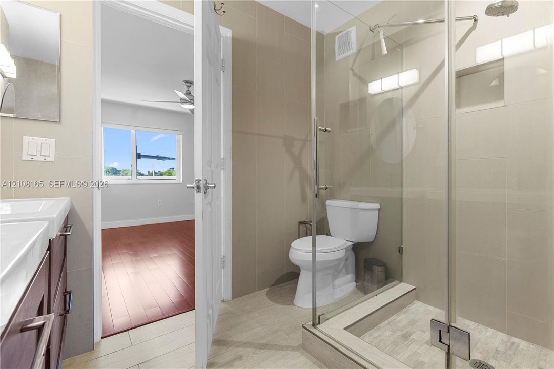Bathroom featuring a glass-enclosed shower with tiled walls, dual-sink vanity with dark cabinetry, tile flooring, and integrated wall-mounted lighting