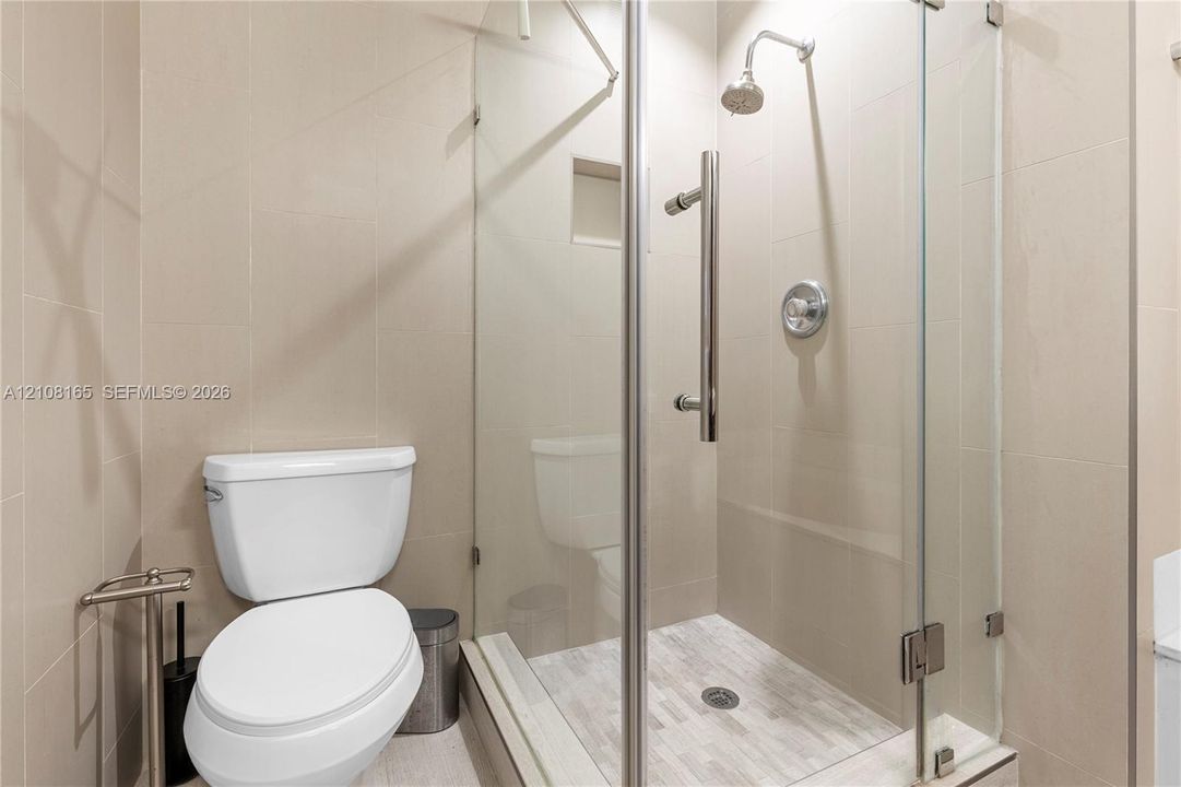 Walk-in shower with frameless glass enclosure, polished metallic fixtures, built-in recessed wall niche, and light-toned wall tile