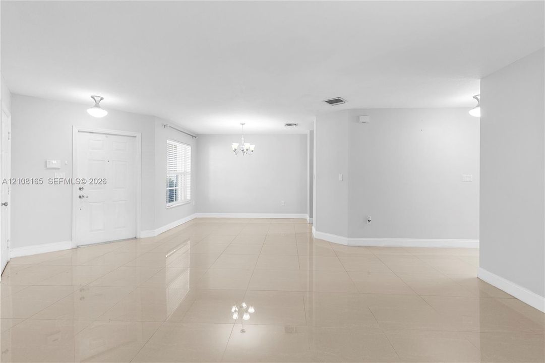 Neutral-toned tile flooring, multi-panel entry door, chandelier lighting, and large window with horizontal blinds