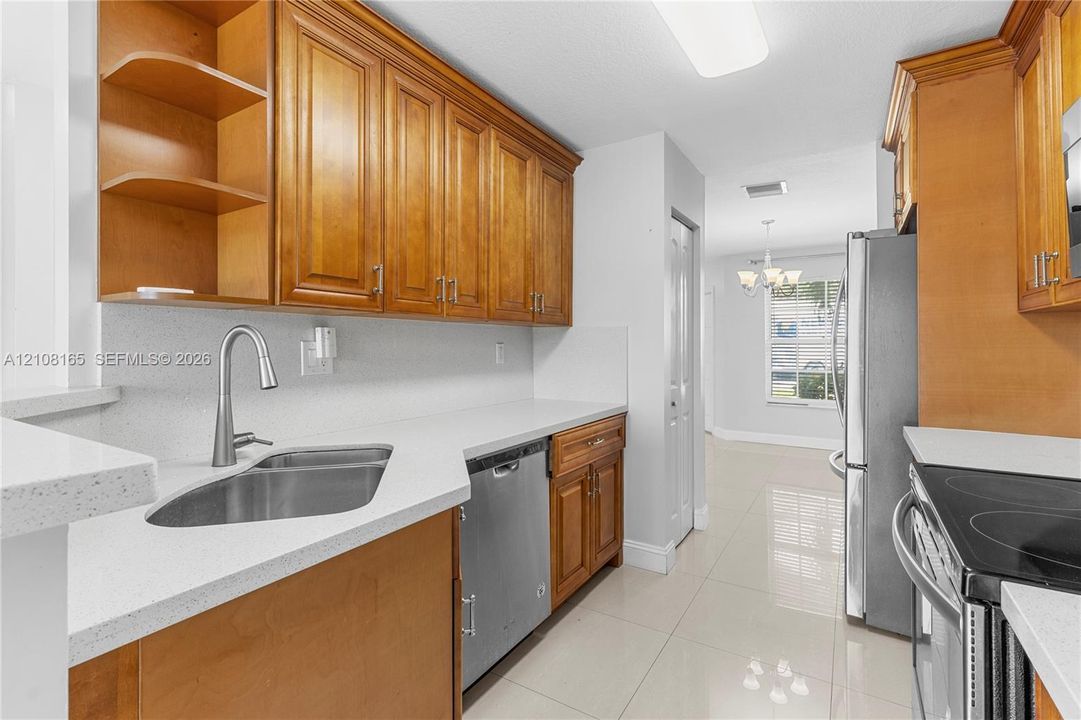 Kitchen featuring wood cabinetry, stainless steel appliances, neutral countertops, a high-arc faucet, and tile flooring