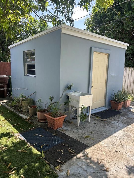 Detached structure featuring a smooth stucco exterior, flat roofline, louvered window, solid-panel entry door, and an exterior utility sink