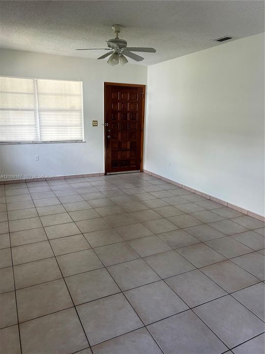 Interior room featuring neutral ceramic tile flooring, a multi-paneled wood-finish door, and a ceiling-mounted light fixture with an integrated fan