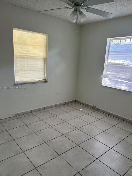 Interior room featuring large-format ceramic tile flooring, two windows with exterior security bars, and a ceiling fan with integrated lighting