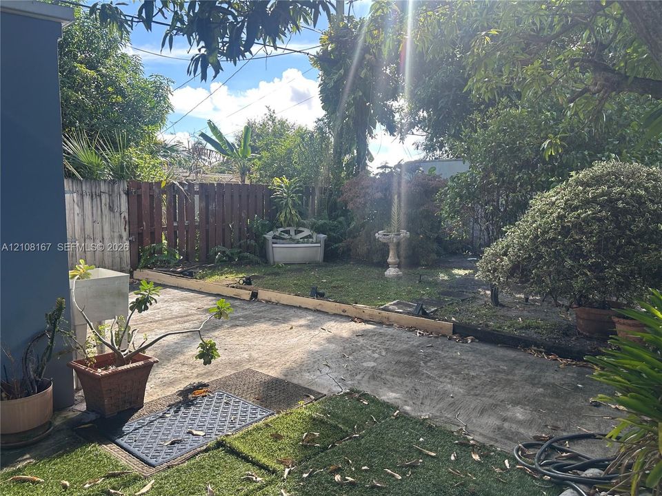 Fenced backyard featuring a concrete patio, synthetic turf area, and mature landscape elements
