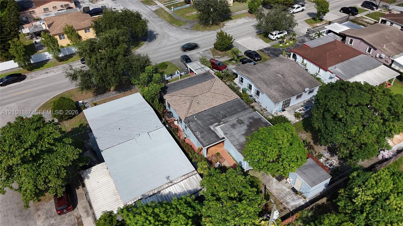 Aerial perspective of a property featuring a multi-section roofline, paved driveway, detached storage structure, and established perimeter vegetation