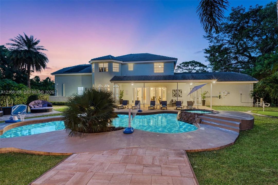Two-story exterior featuring a hip roof, covered rear patio, freeform swimming pool, integrated spa, and stone-paver hardscaping