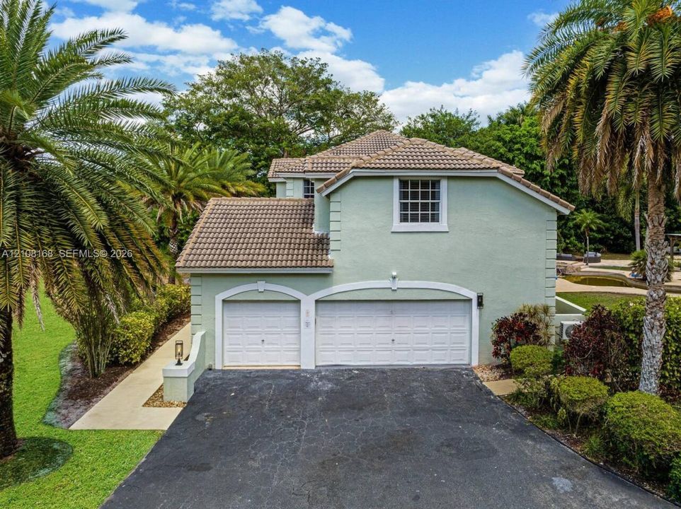 Two-story stucco exterior featuring a tiled roof, arched double-garage door entries, and multi-pane windows