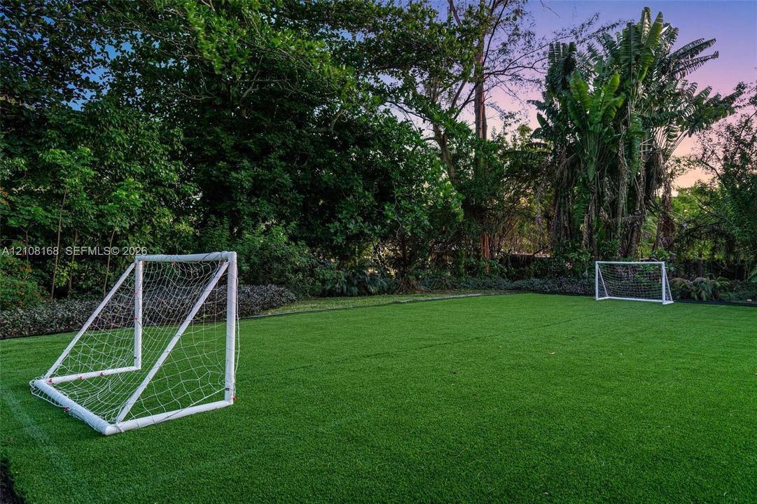 Expansive lawn featuring artificial turf, mature tree border, and perimeter landscaping