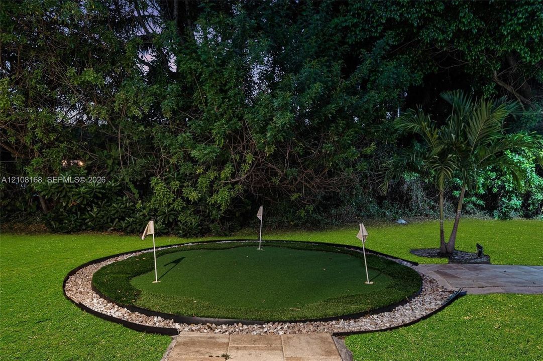 Backyard putting green featuring three flag pins, synthetic turf surface, stone border edging, and stone paver walkway