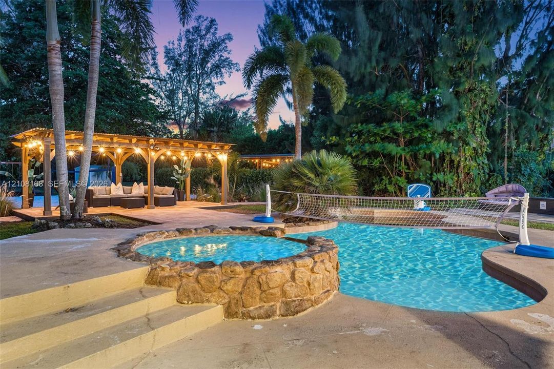 Outdoor space featuring a swimming pool, an integrated spa with stone masonry, a wood-frame pergola, and concrete decking