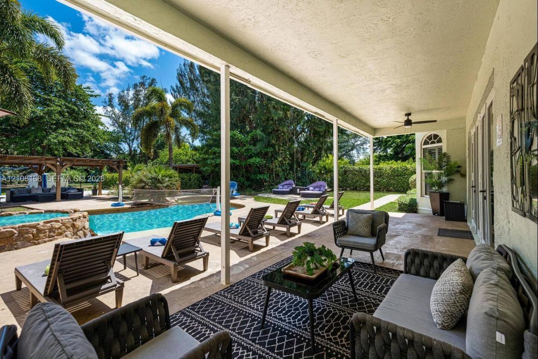 Covered outdoor patio featuring natural stone flooring, a ceiling fan, a swimming pool with rock-style water feature, and a wooden pergola structure