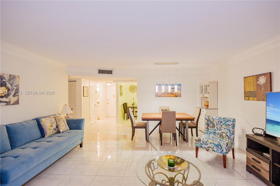 Open-concept living space featuring large-format tile flooring, crown molding, a built-in cabinetry unit, and a linear multi-pendant light fixture