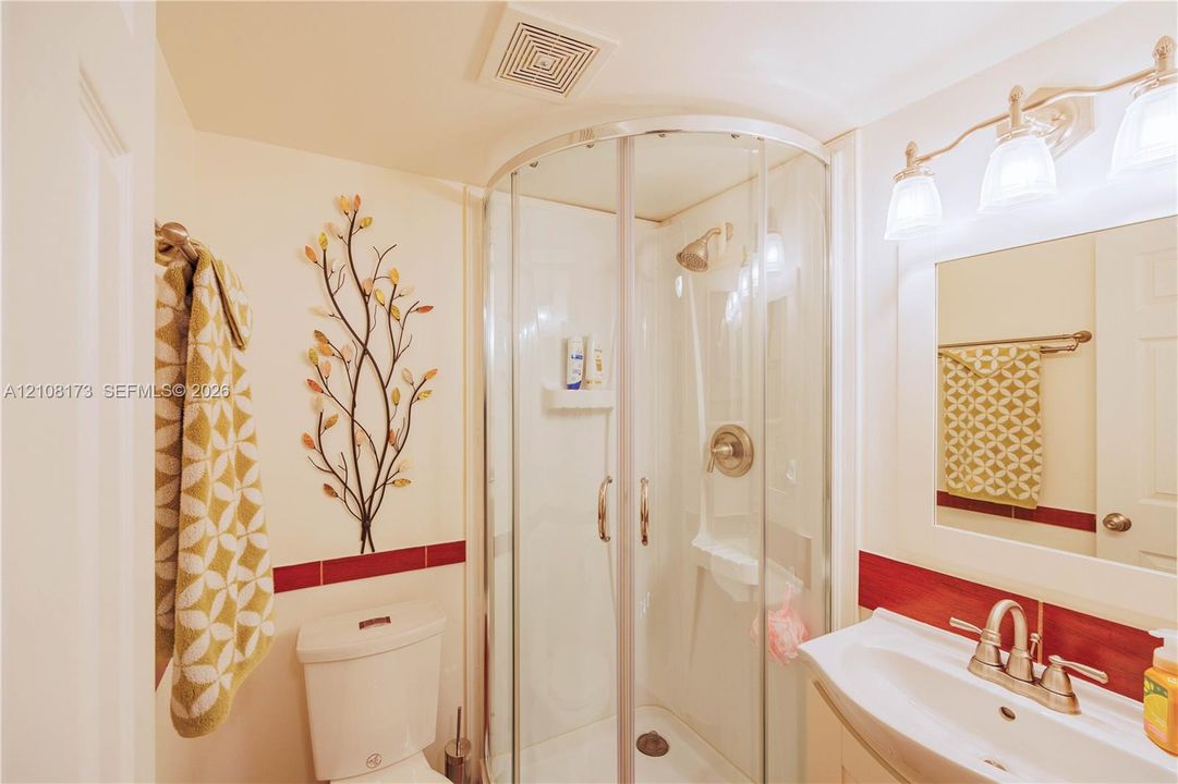 Curved glass corner shower enclosure featuring a metal-finish faucet, white vanity with an integrated sink, metal-finish widespread faucet, and multi-light vanity fixture