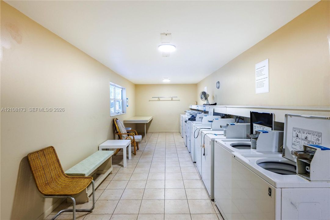 Laundry facility featuring rows of multiple side-by-side washers and dryers, tile flooring, flush-mount ceiling lighting, and a built-in folding surface