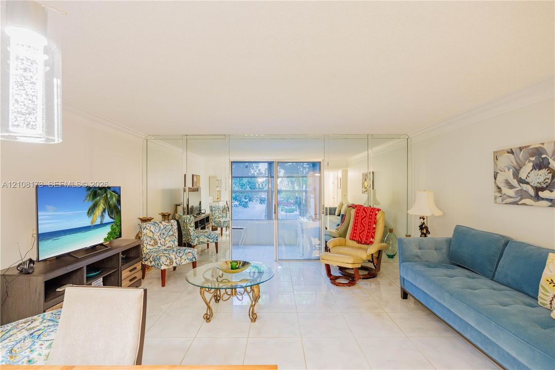 Living area featuring large-format ceramic tile flooring, floor-to-ceiling mirrored wall paneling, crown molding, and sliding glass doors