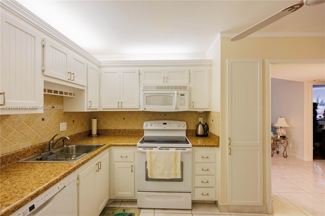 Kitchen featuring white shaker-style cabinetry, stone-finish countertops, diagonal tile backsplash, built-in microwave, and tile flooring