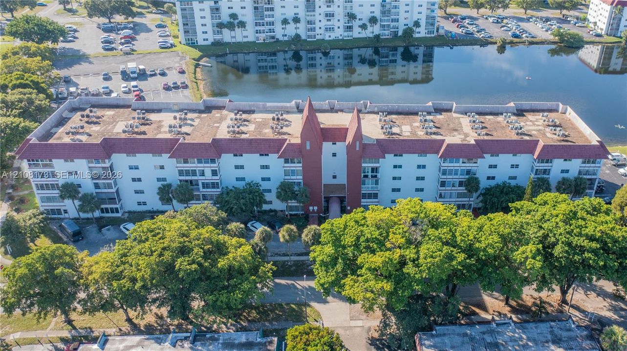 Multi-story residential building featuring a prominent gabled roofline, tile roofing, stucco exterior, and waterfront placement