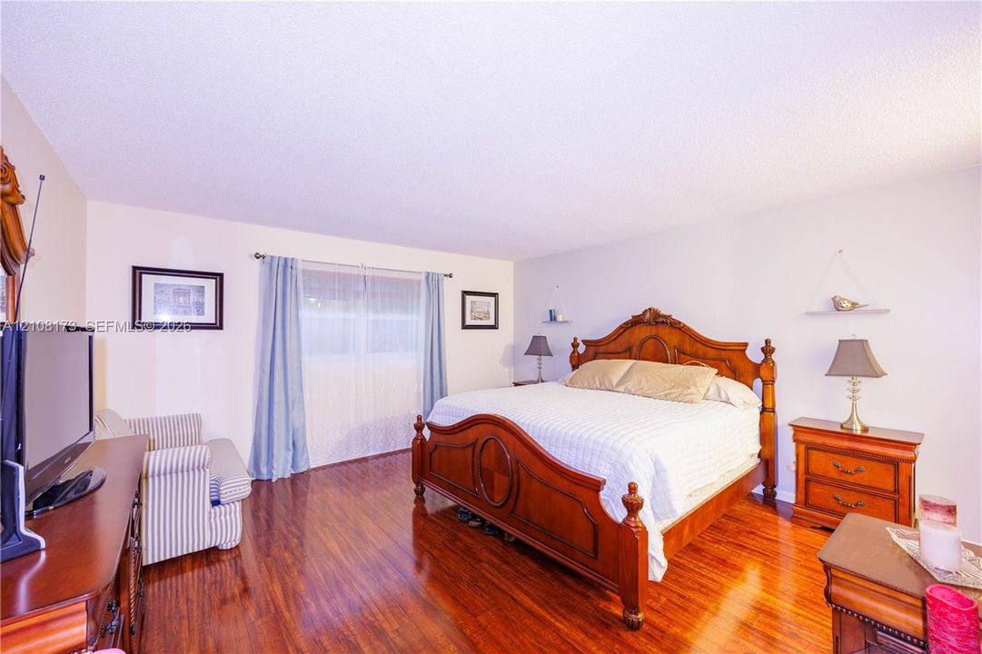 Spacious room featuring wood-finish flooring, textured ceiling, and large window with dual-rod hardware