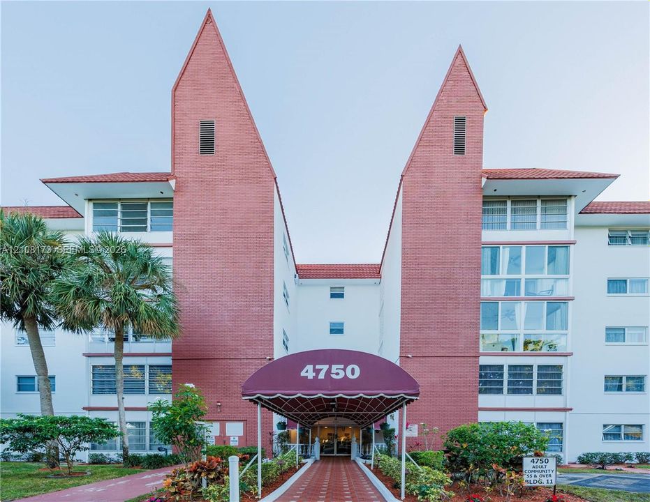 Multi-story exterior featuring a red brick facade, distinctive peaked roofline, a covered entrance canopy, and horizontal window rows