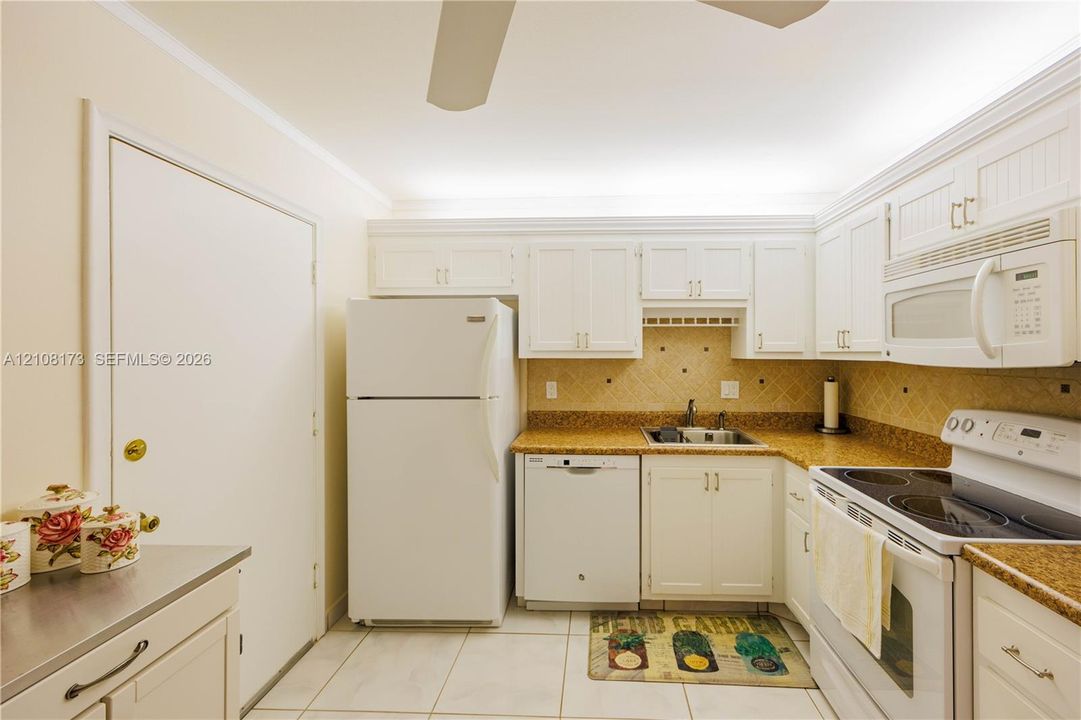 Kitchen featuring white cabinetry, stone-finish countertops, tiled backsplash, built-in appliances, and ceramic tile flooring