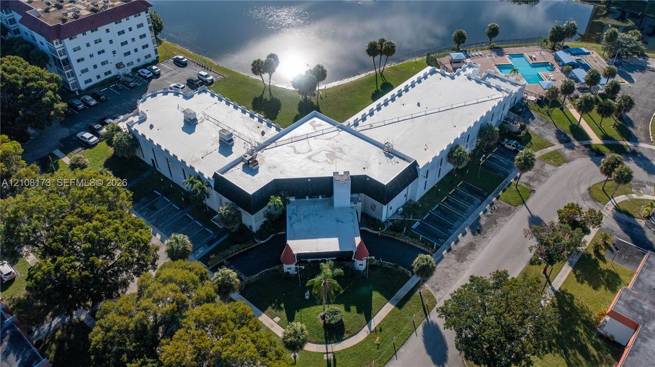 Aerial perspective of a multi-story building featuring a flat roofline, turret-style architectural accents, onsite parking areas, and grounds with mature palm trees