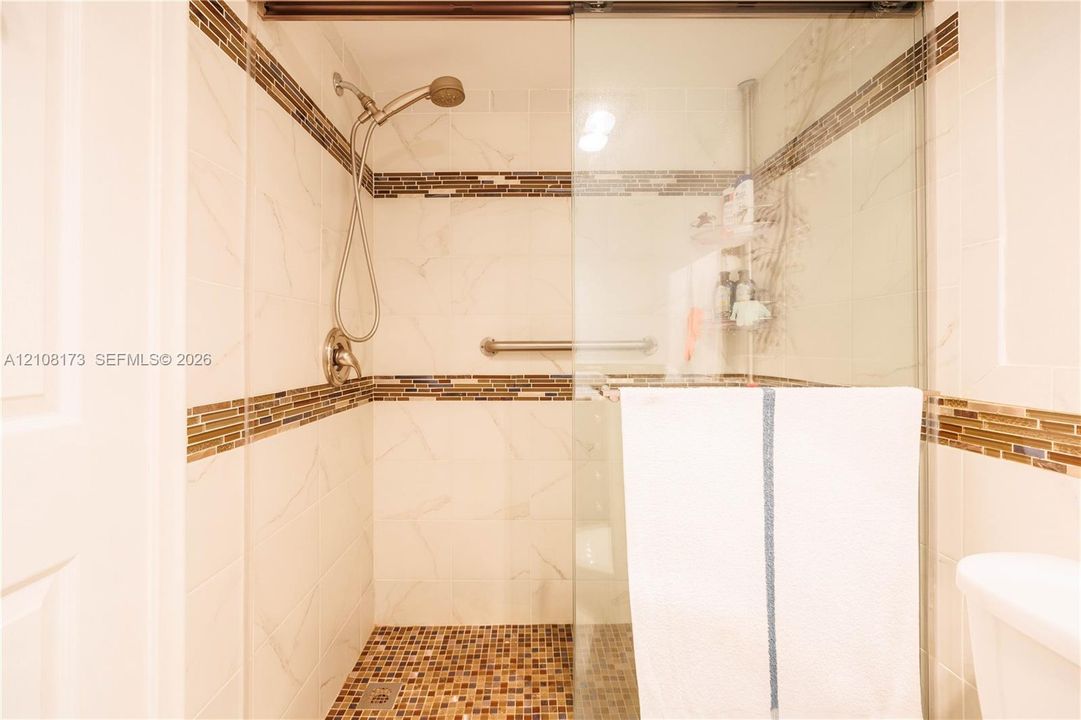 Walk-in shower featuring glass sliding doors, stone-tiled floor, decorative horizontal accent tile, and a wall-mounted showerhead