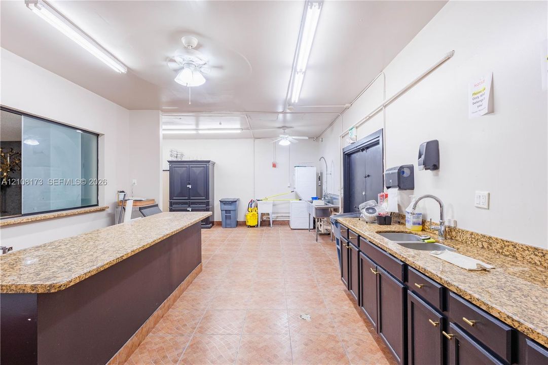 Large multi-purpose room featuring stone-finish countertops, dark cabinetry, dual-basin stainless steel sink, tile flooring, and ceiling-mounted linear lighting