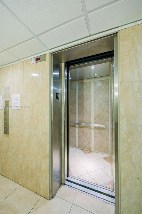 Elevator featuring a stainless steel frame, polished stone-finish wall cladding, recessed ceiling lighting, and a horizontal metal handrail