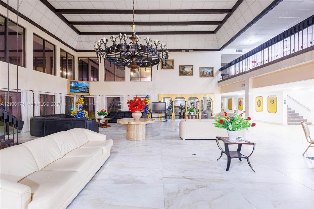 Expansive living area featuring vaulted ceilings with exposed beams, large-scale tile flooring, a multi-tiered iron chandelier, and an open-concept mezzanine railing