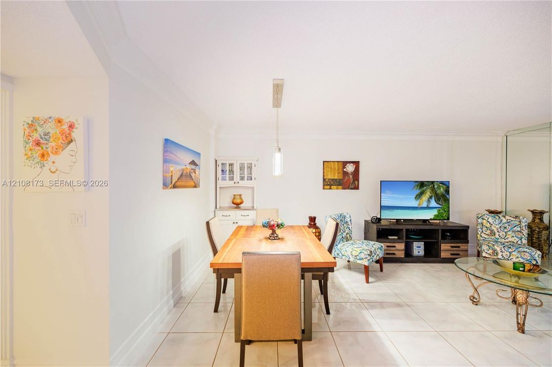Open-concept interior featuring light-toned tile flooring, built-in white cabinetry with glass-paneled upper doors, a singular pendant light fixture, and floor-to-ceiling mirrored wall paneling