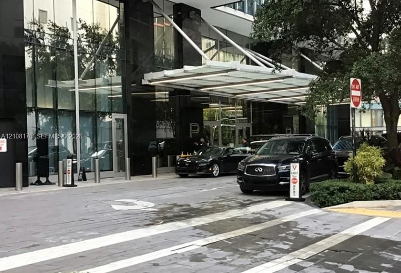 Contemporary building exterior featuring a polished black stone facade, expansive floor-to-ceiling glass paneling, and a cantilevered architectural canopy over a paved motor court
