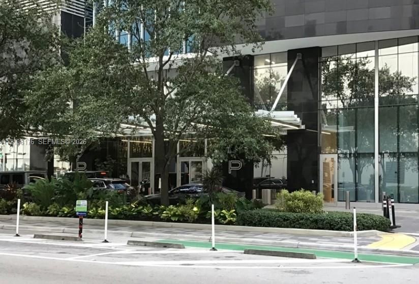 Modern glass-and-stone facade featuring a covered porte-cochère, floor-to-ceiling glass paneling, and polished dark stone accents