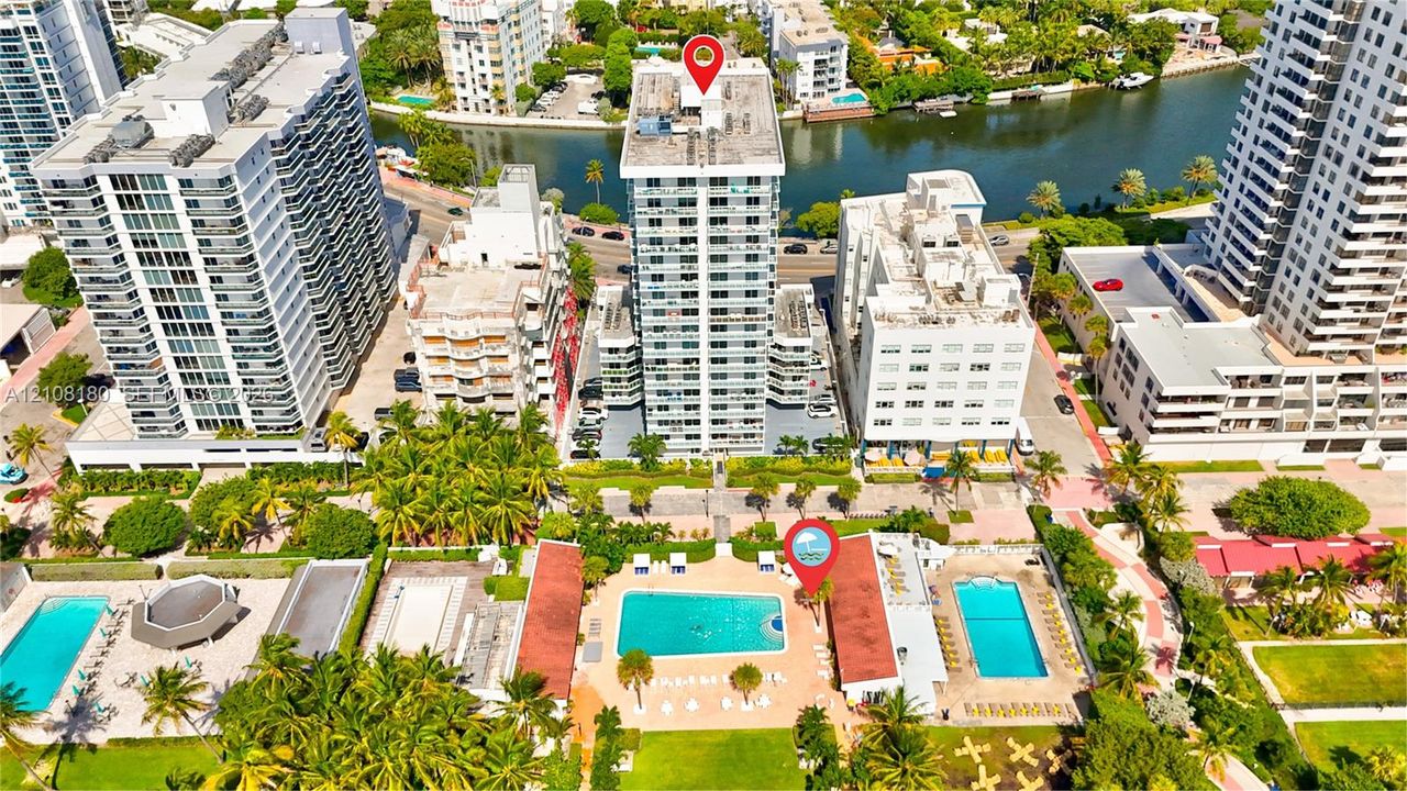 High-rise residential building featuring exterior balconies, a ground-level swimming pool, and tropical landscaping situated along a waterway