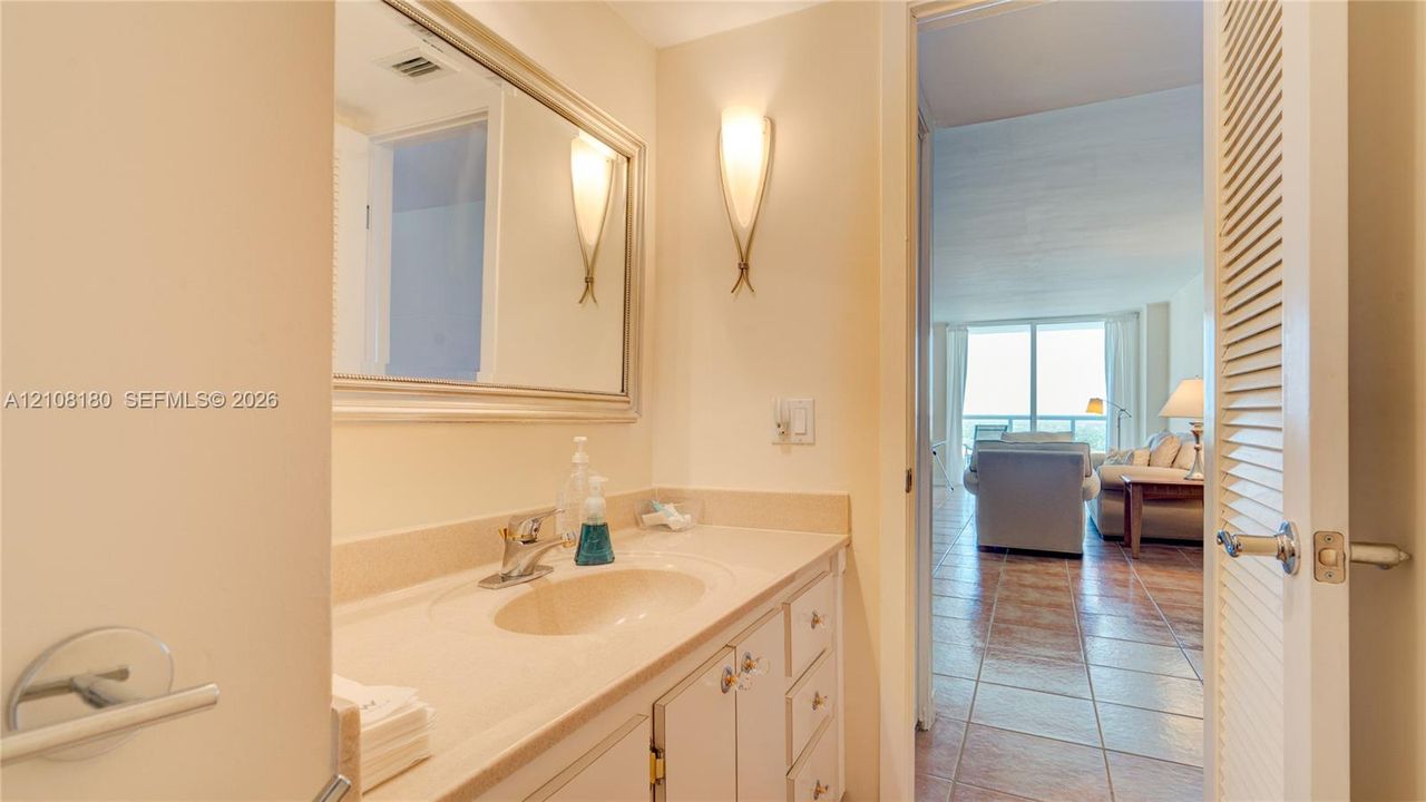 Vanity with integrated sink and countertop, framed wall mirror, dual wall-mounted sconces, and louvered-style closet door