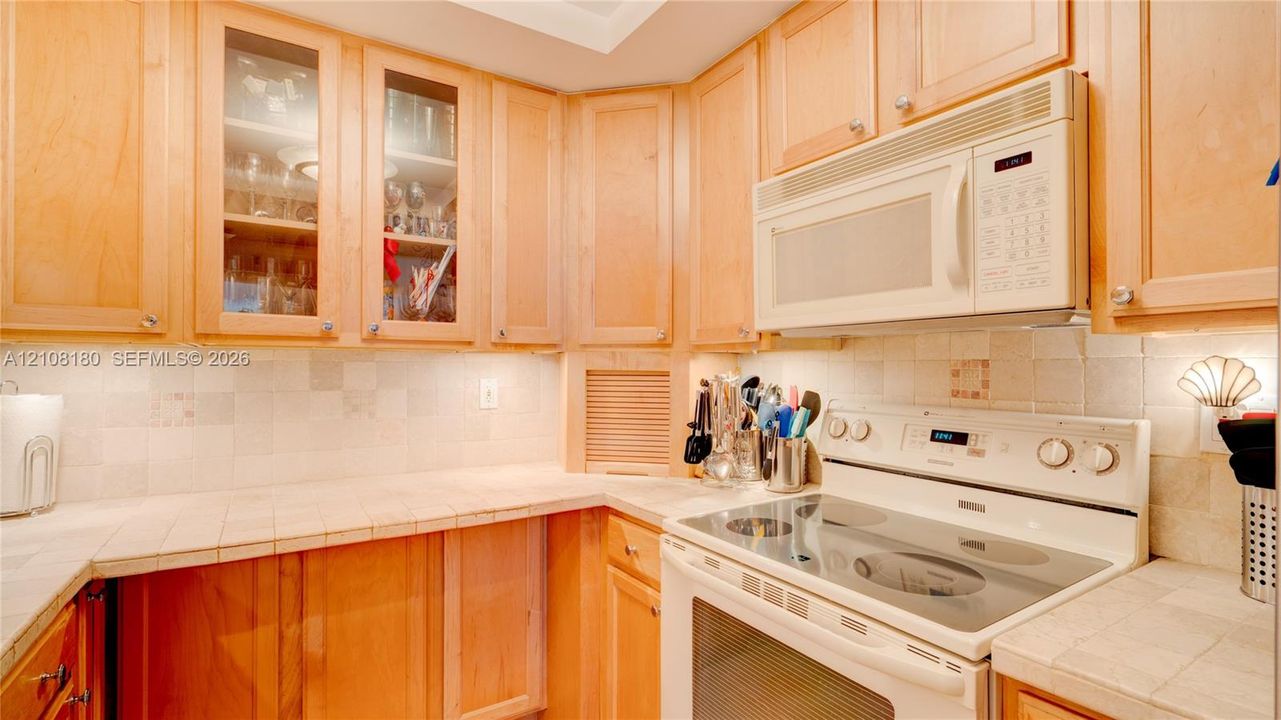 Kitchen featuring natural wood cabinetry, glass-front upper display cabinets, tile backsplash, tile countertops, and integrated over-the-range microwave