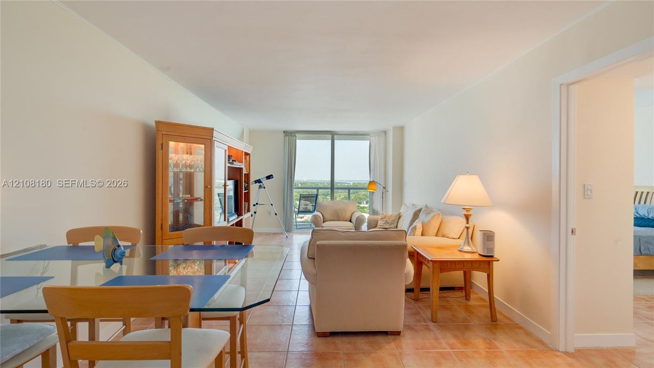 Open-concept interior featuring neutral wall tones, large-format tile flooring, and floor-to-ceiling glass doors leading to a private balcony