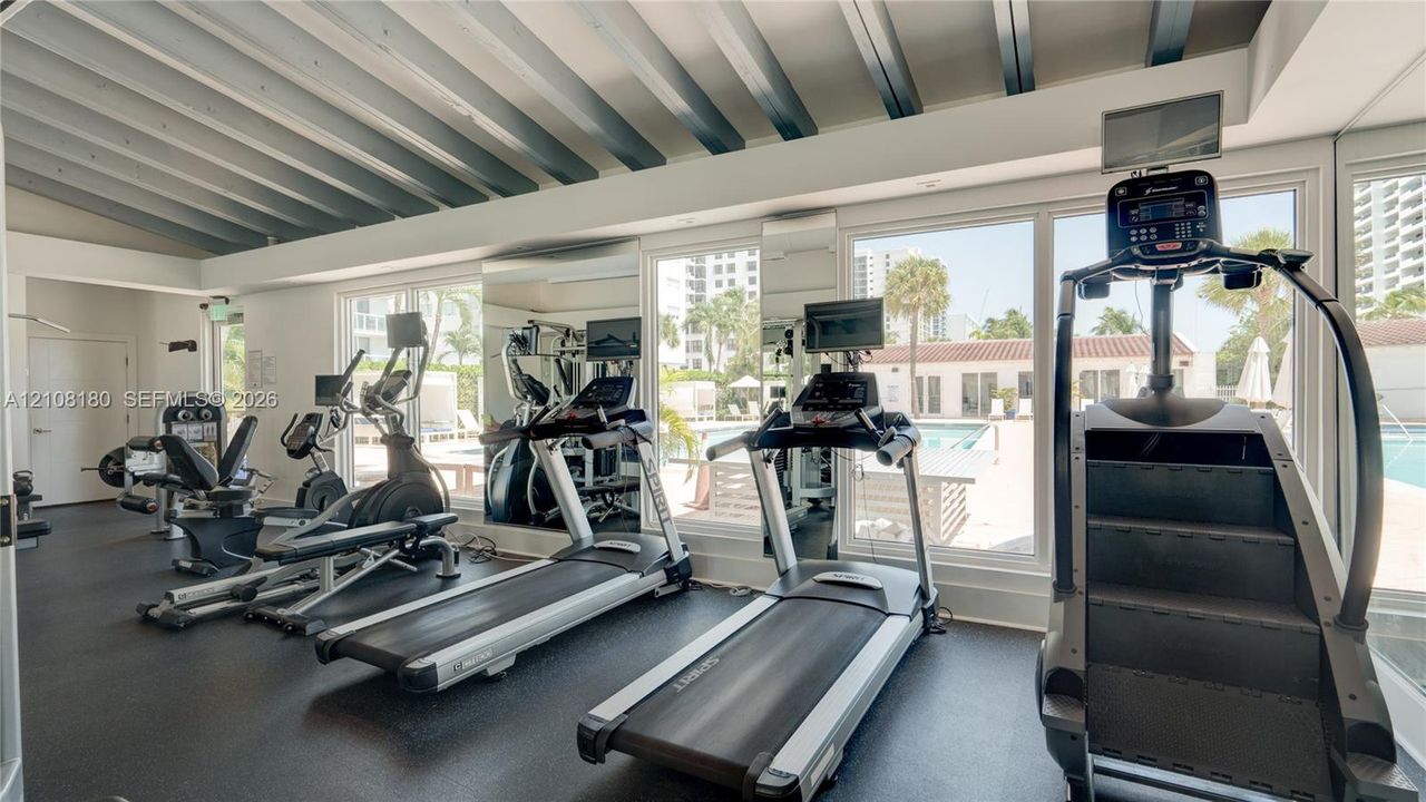 Fitness center featuring a vaulted ceiling with exposed beams, wall-to-wall mirrors, and floor-to-ceiling windows